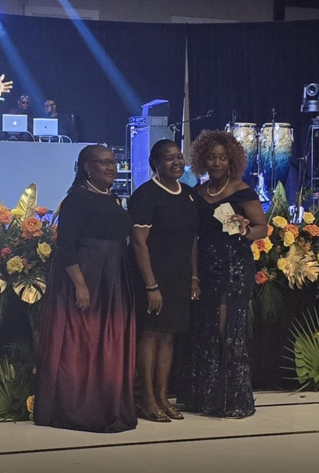 Three women posing together on a decorated stage with flowers and musical instruments.